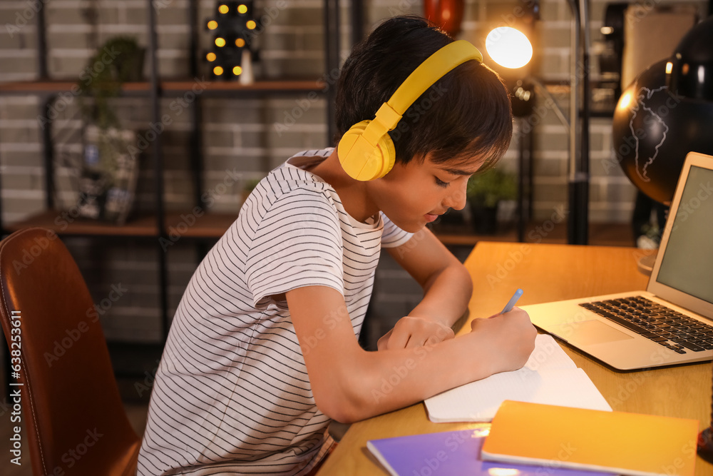 Little boy with headphones studying at home late in evening