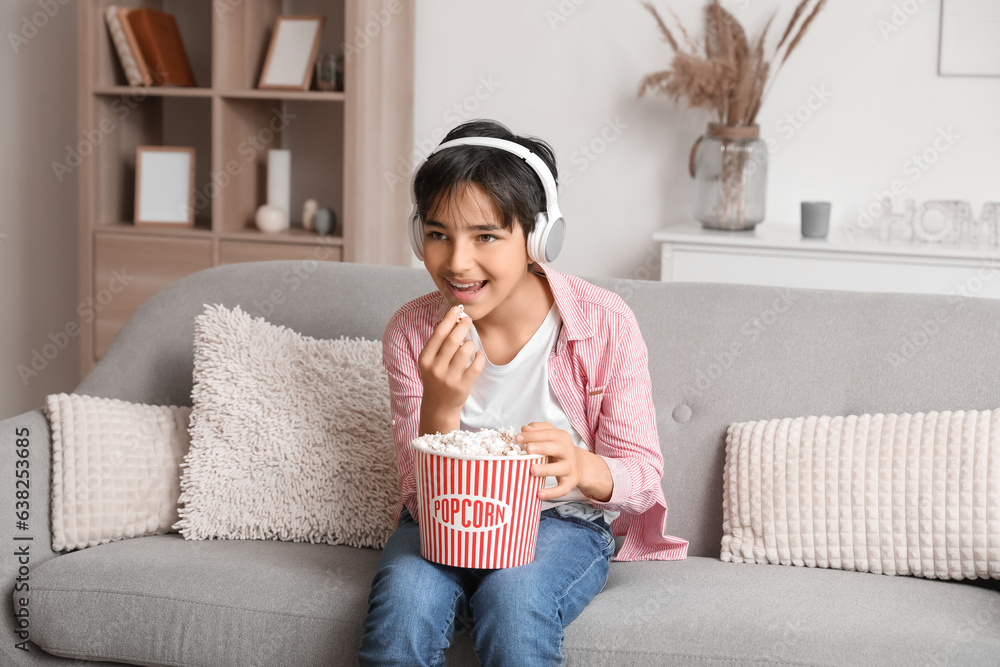 Little boy in headphones with popcorn watching movie at home