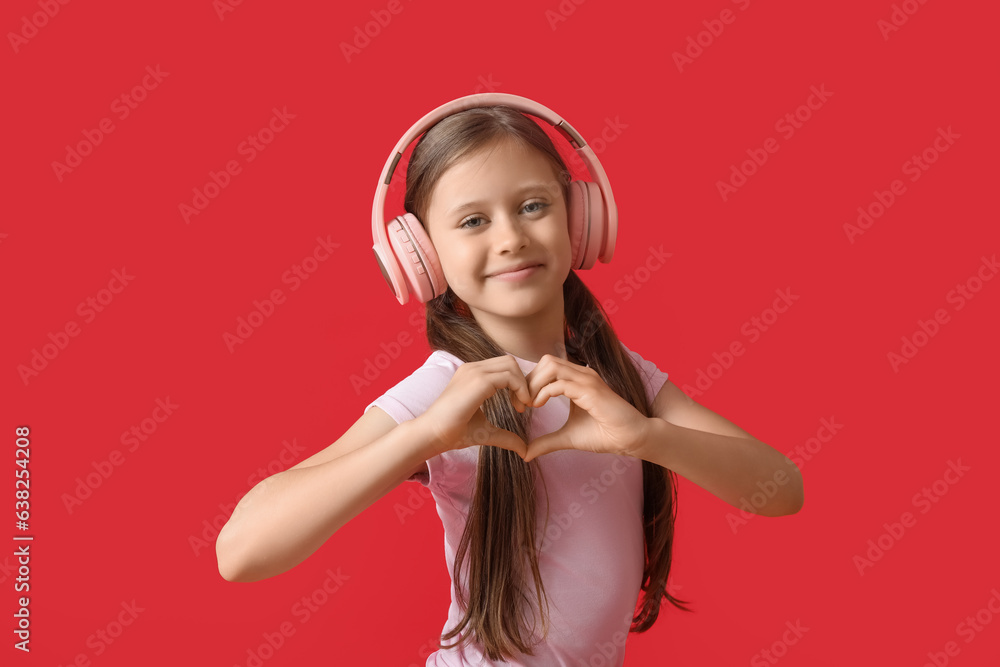 Little girl in headphones making heart gesture on red background