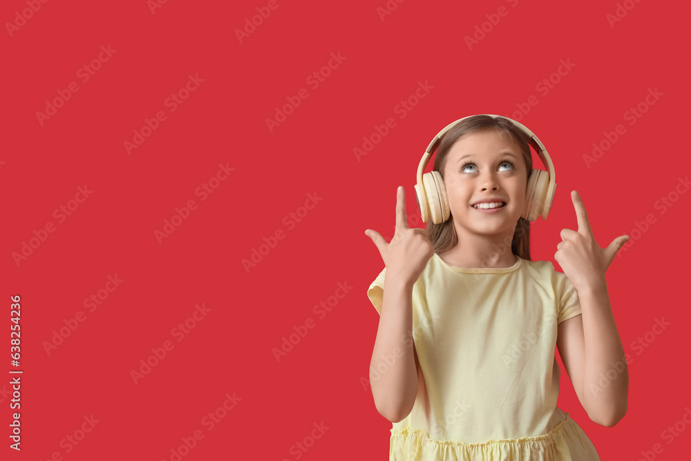 Little girl in headphones pointing at something on red background