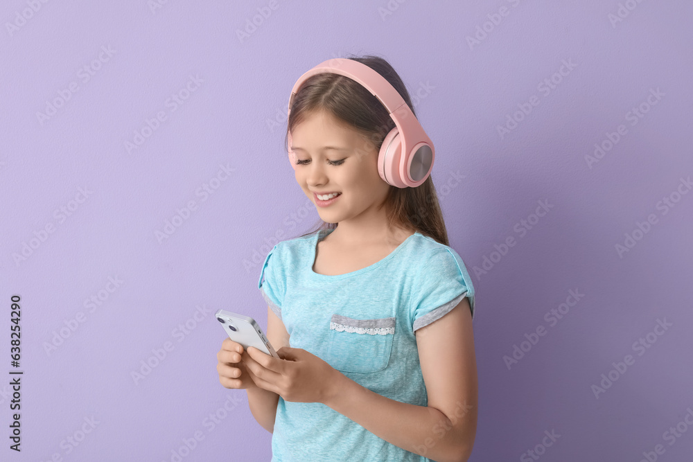 Little girl in headphones using mobile phone on lilac background