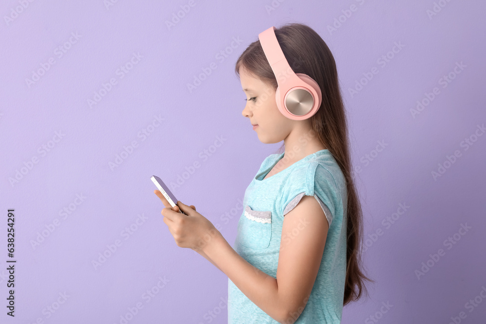 Little girl in headphones using mobile phone on lilac background