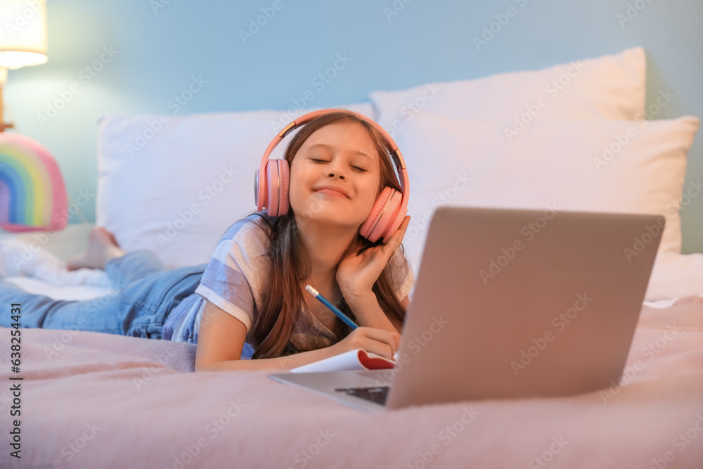 Little girl with headphones studying online in bedroom at night