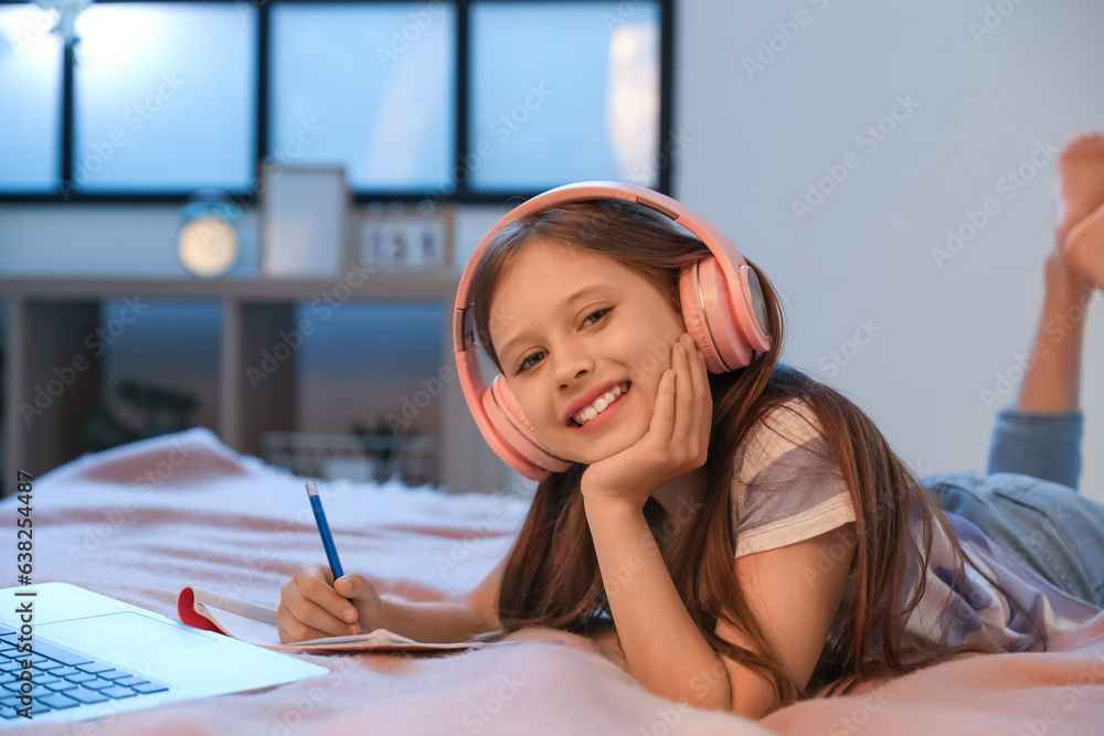 Little girl with headphones studying online in bedroom at night