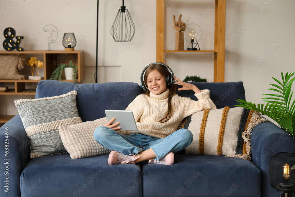 Little girl in headphones using tablet computer at home