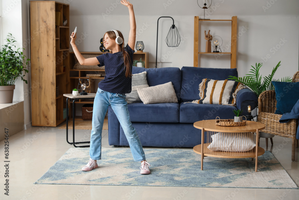 Little girl in headphones with mobile phone dancing at home