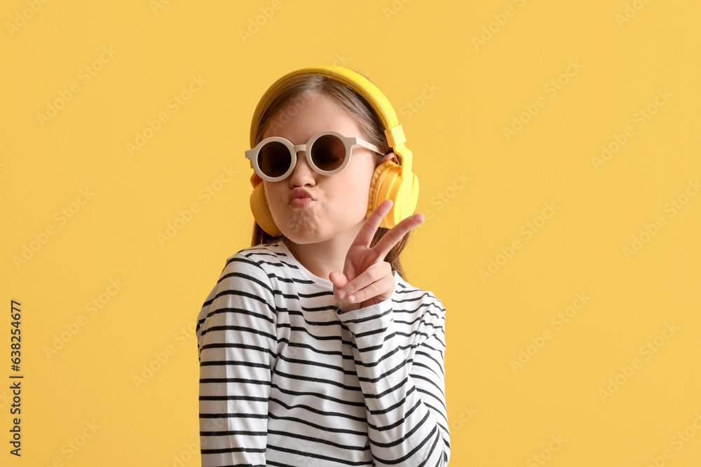 Little girl in headphones showing victory gesture on yellow background, closeup