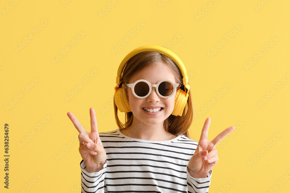 Little girl in headphones showing victory gesture on yellow background, closeup