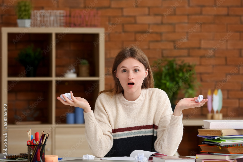 Shocked teenage girl with crunched paper doing lessons at home