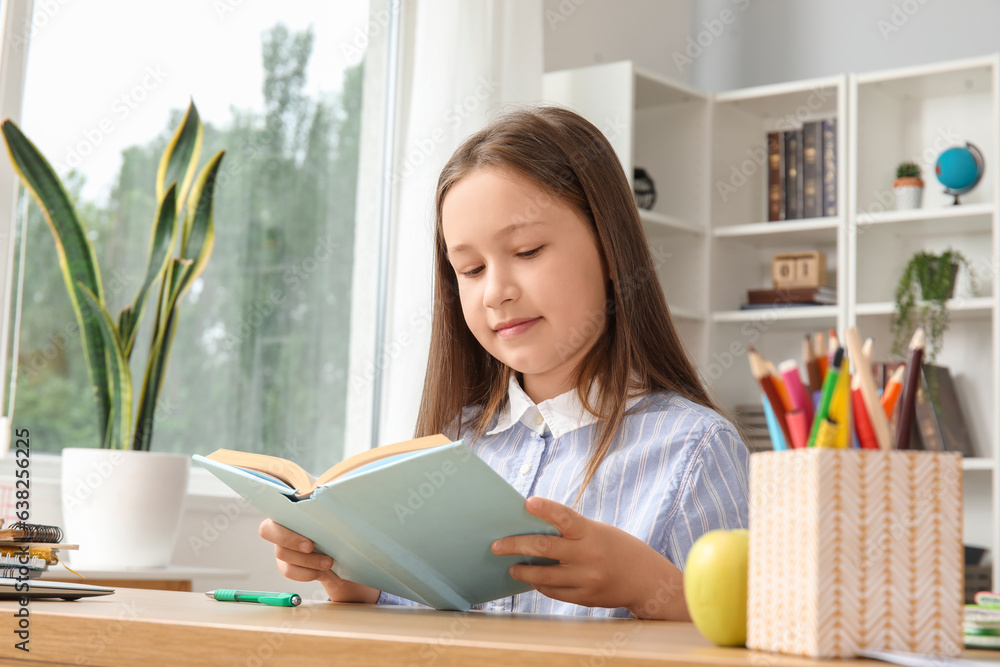 Cute little girl reading schoolbook at home