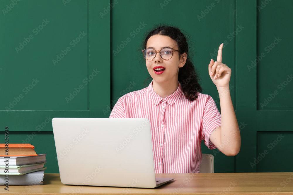 Female student with laptop pointing at something near green wall