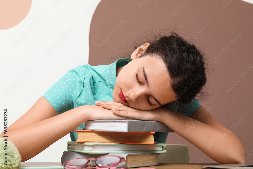 Tired female student sleeping after doing homework at table near color wall