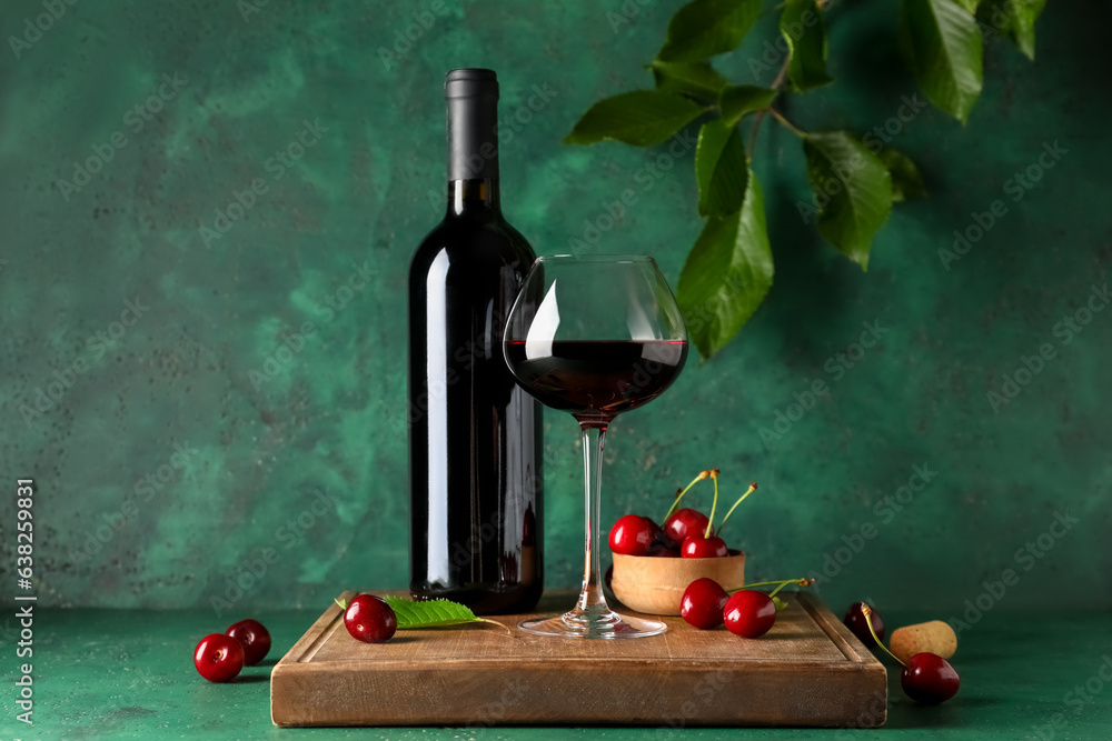 Glass and bottle of sweet cherry liqueur with berries on wooden board near green wall