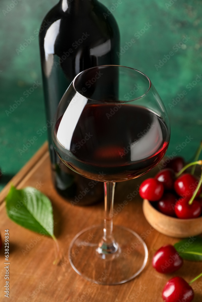 Glass and bottle of sweet cherry liqueur with berries on wooden board near green wall