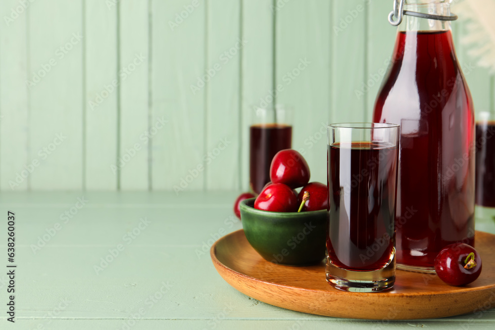 Bottle and glasses of sweet cherry liqueur with berries on green wooden table near wall