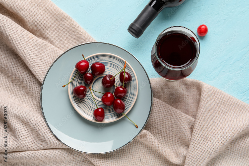 Bottle and glass of sweet cherry liqueur with berries on blue background