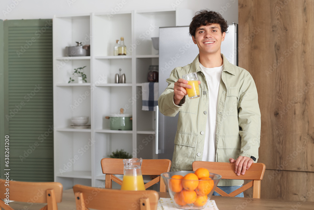 Young man with glass of orange juice in kitchen