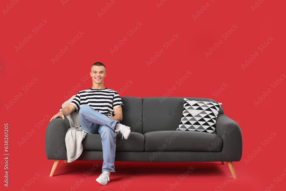 Happy young man sitting on sofa against red background