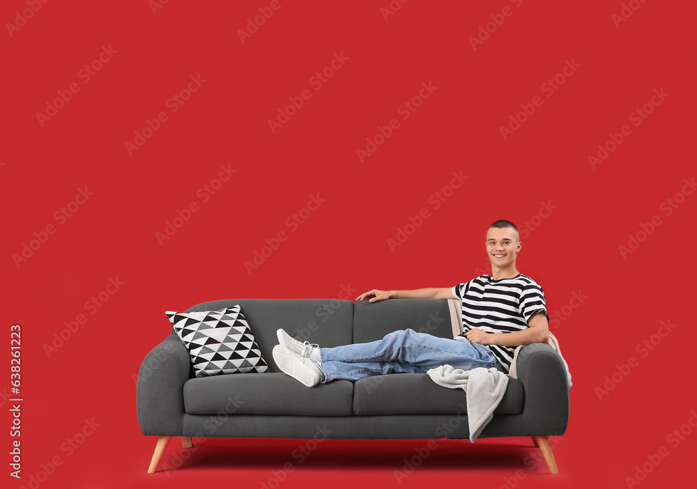 Happy young man sitting on sofa against red background