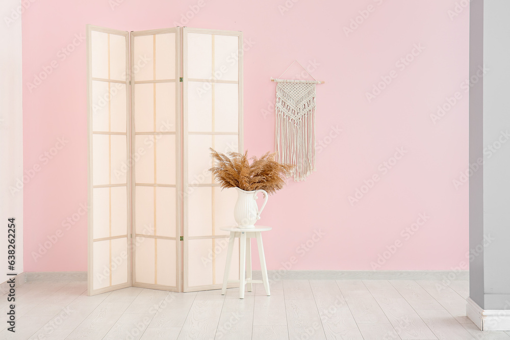 Folding screen, stool and vase of dried flowers near pink wall