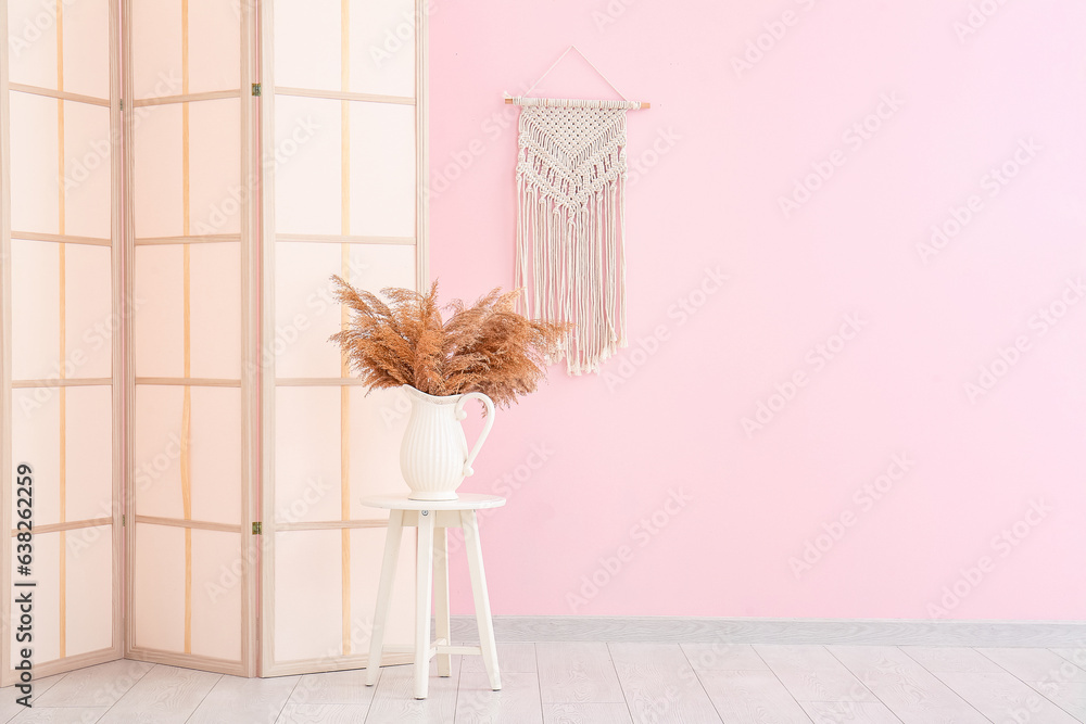 Folding screen, stool and vase of dried flowers near pink wall