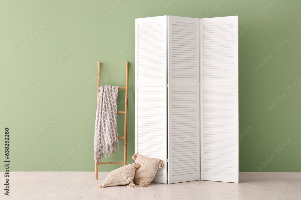 Folding screen, ladder and pillows near green wall