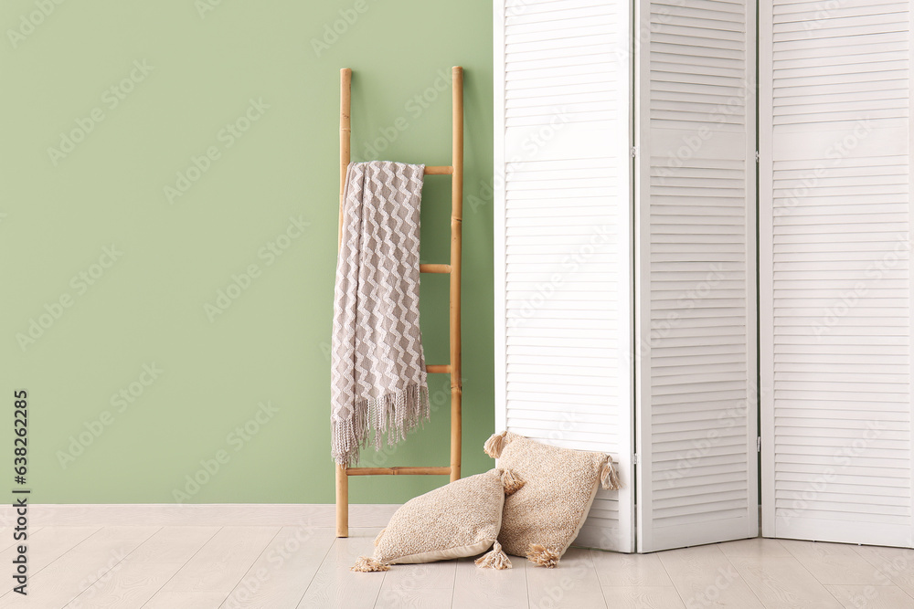 Folding screen, ladder and pillows near green wall