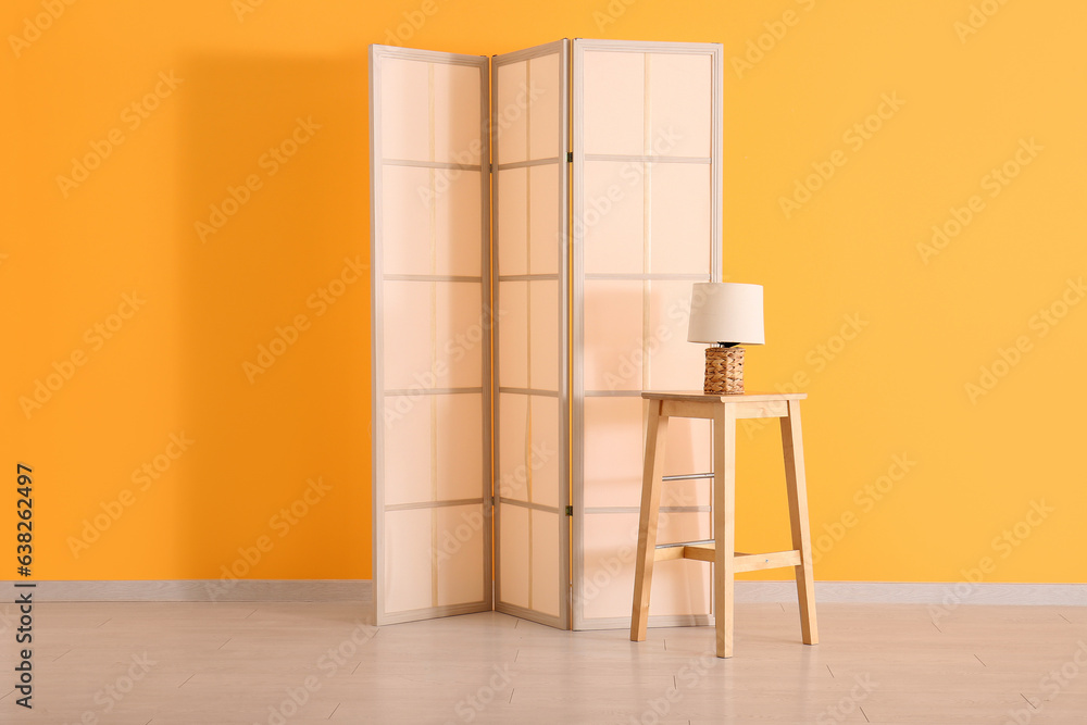 Folding screen, table and lamp near orange wall