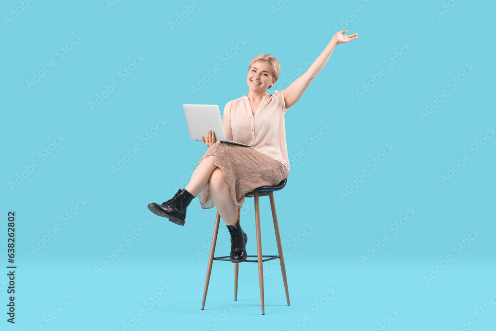 Happy young female programmer with laptop sitting on chair against blue background