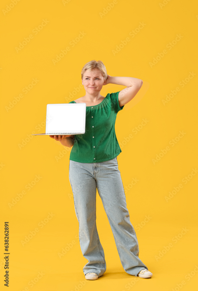 Thoughtful young female programmer with laptop on yellow background