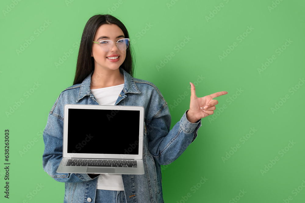 Happy female programmer with laptop pointing at something on green background