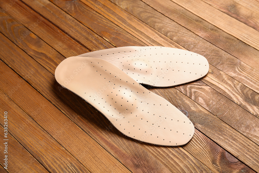 Pair of leather orthopedic insoles on wooden background