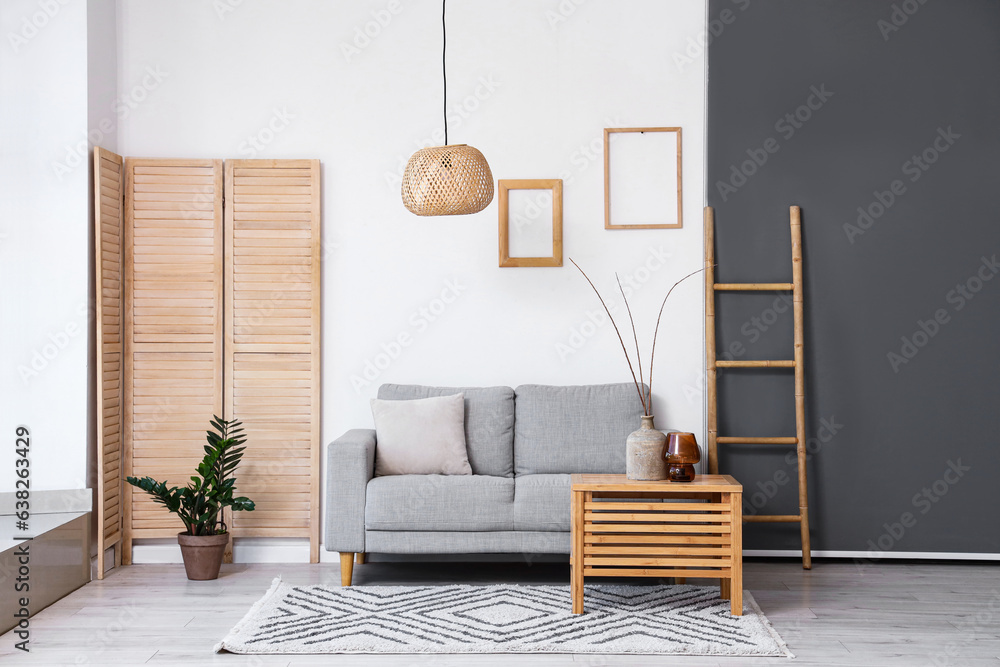 Interior of light living room with grey sofa and branches in vase on wooden table