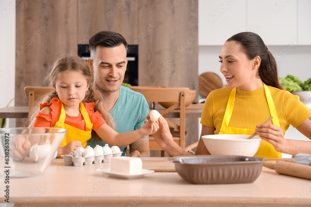 Happy parents with their little daughter preparing dough in kitchen