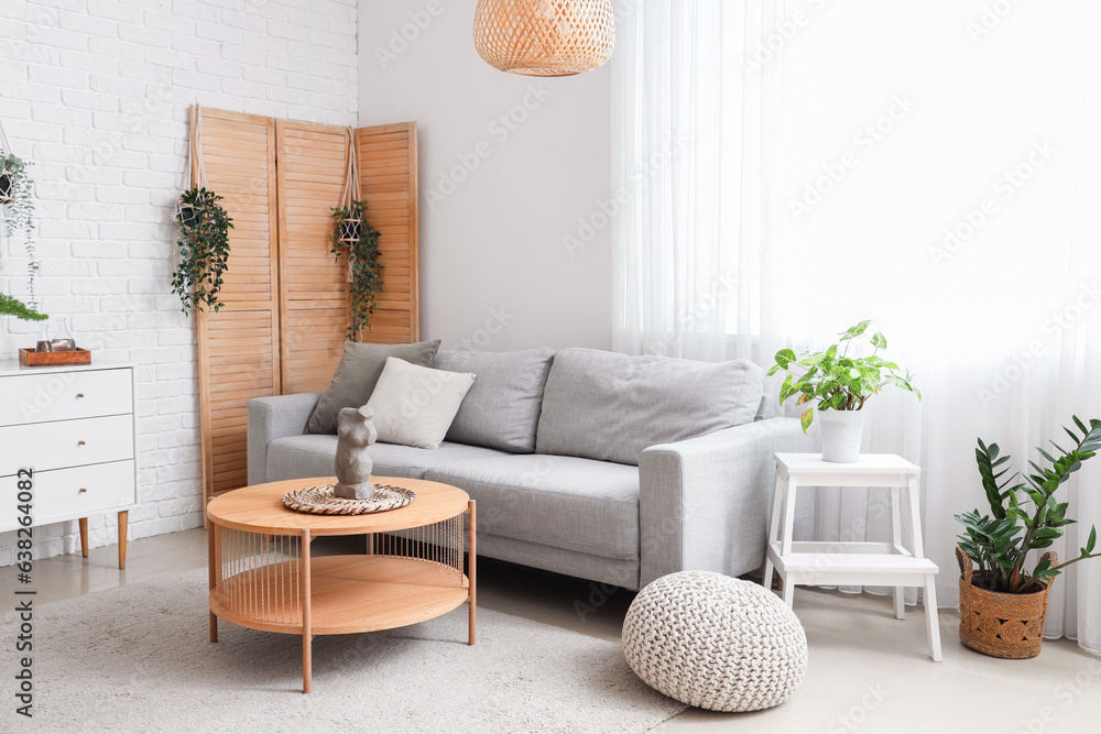 Interior of light living room with grey sofa, wooden coffee table and houseplants