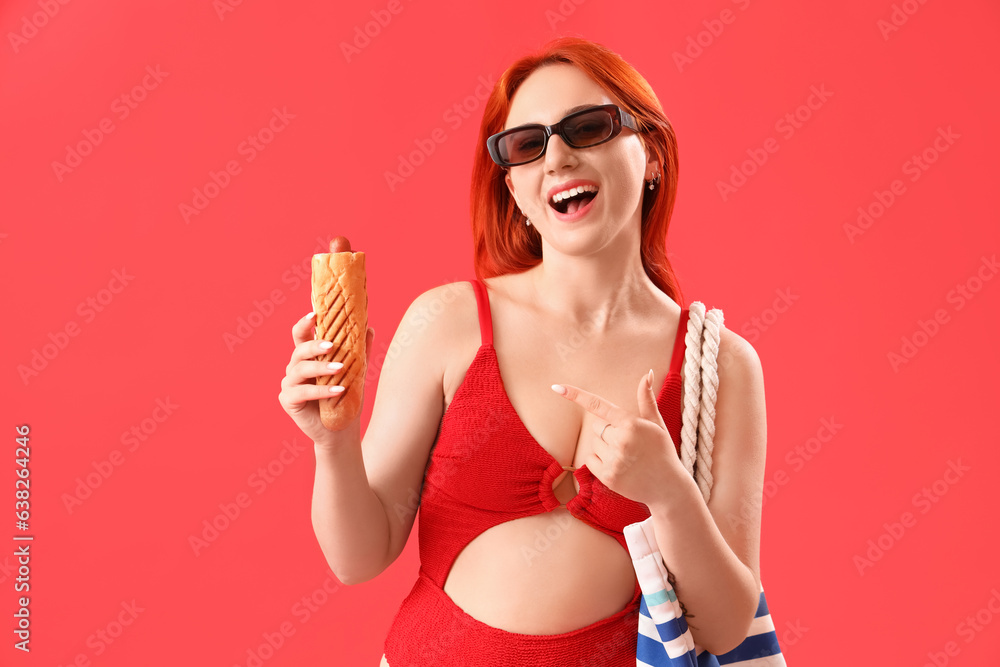 Beautiful young woman in swimsuit, with beach bag and french hot dog on red background