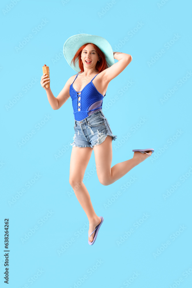 Beautiful jumping young woman with french hot dog on blue background