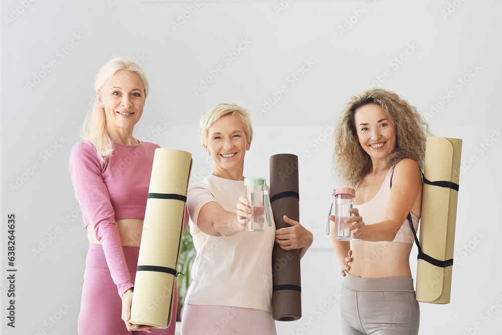 Sporty mature women with yoga mats and bottles of water in gym