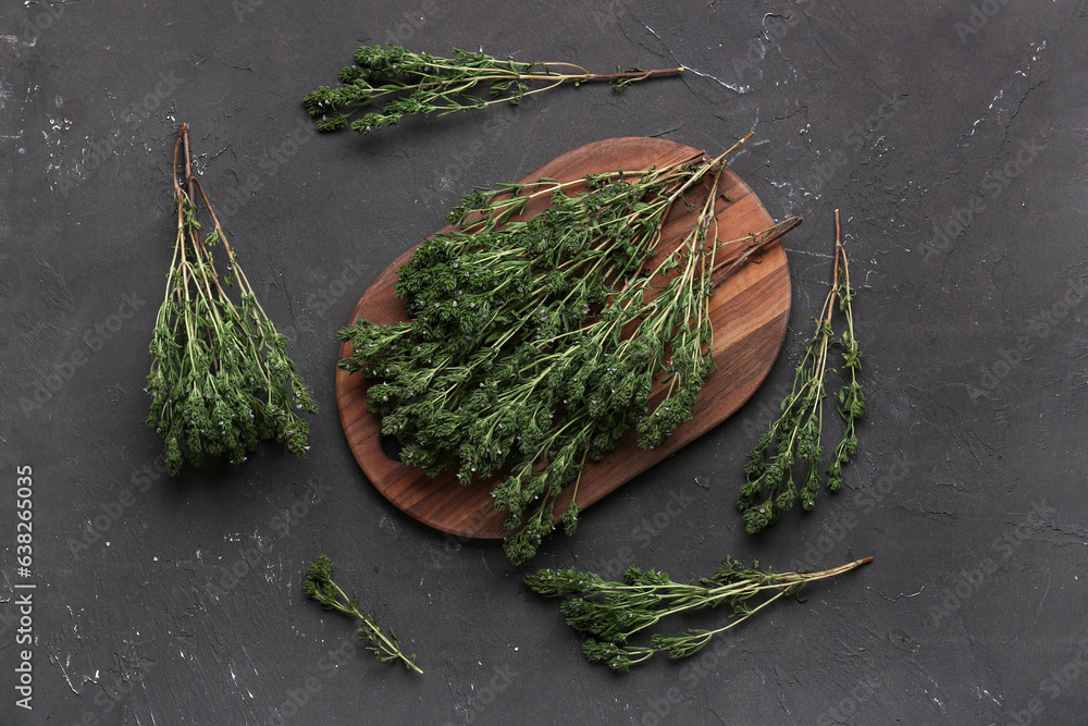 Wooden board with fresh thyme on dark background