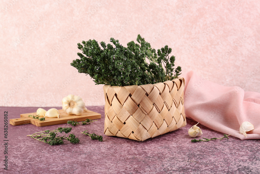 Wicker basket with fresh thyme and garlic on color background