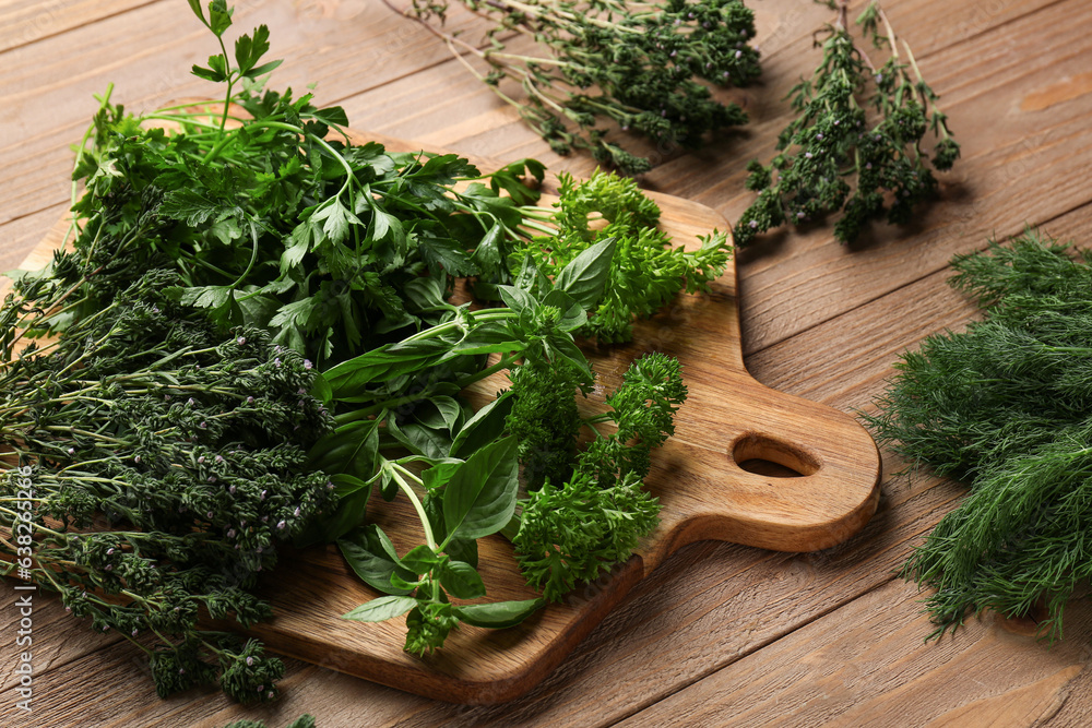 Cutting board with different fresh herbs on wooden background, closeup