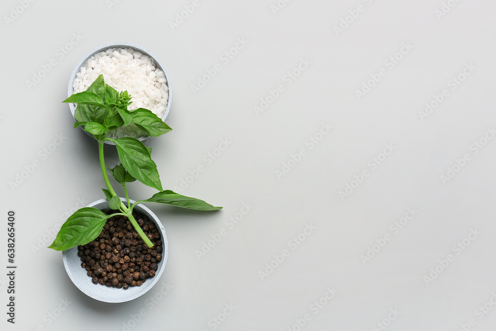 Bowls of sea salt, peppercorns and basil on grey background