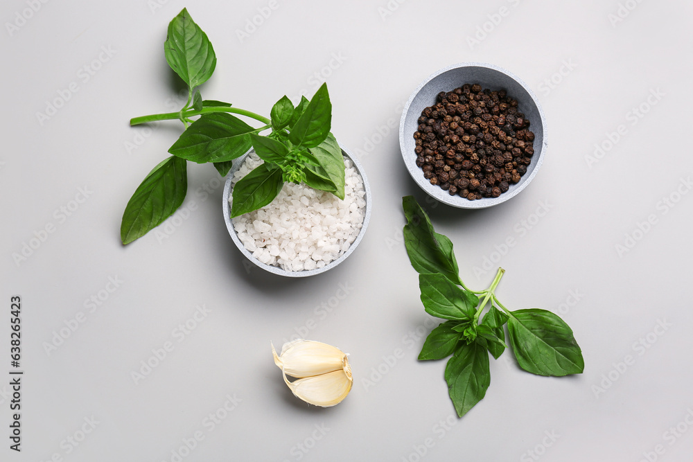 Bowls of sea salt, peppercorns, garlic and basil on grey background