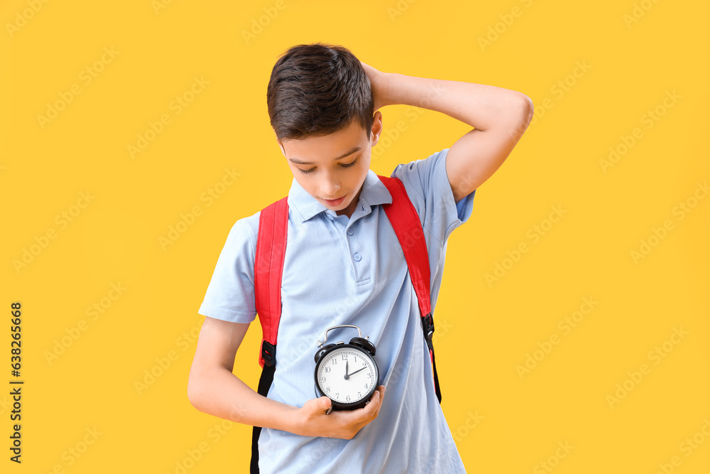 Portrait of thoughtful schoolboy with alarm clock on orange background