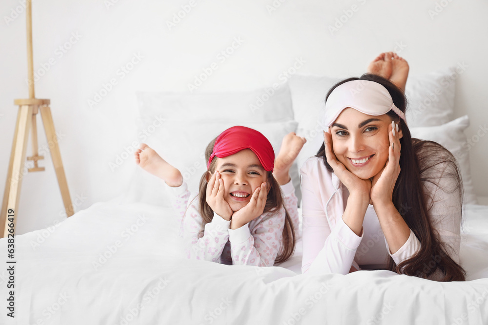 Happy mother and her little daughter with sleeping masks in bedroom