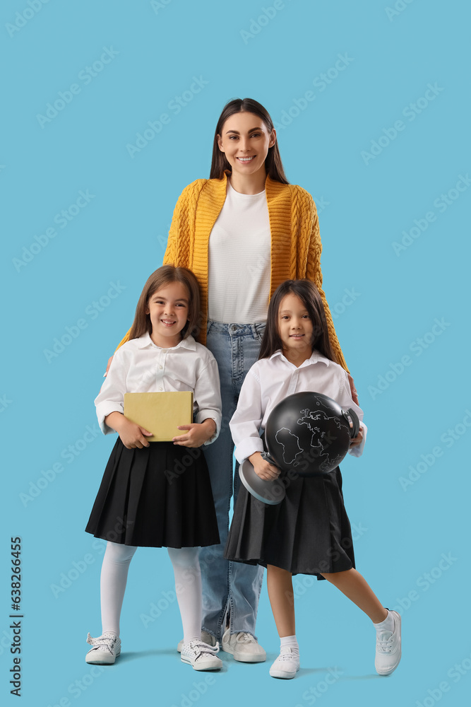 Little school girls with female teacher on light blue background