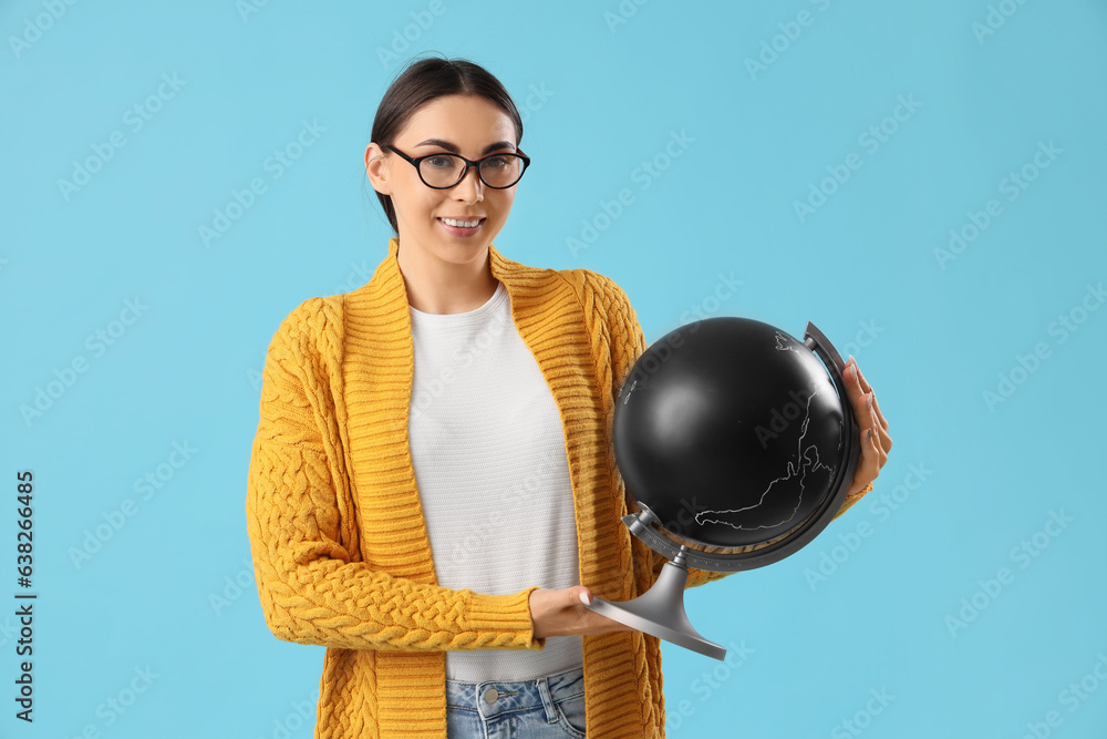 Young female teacher with globe on light blue background