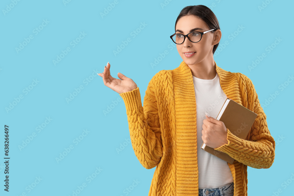 Young female teacher with book on light blue background