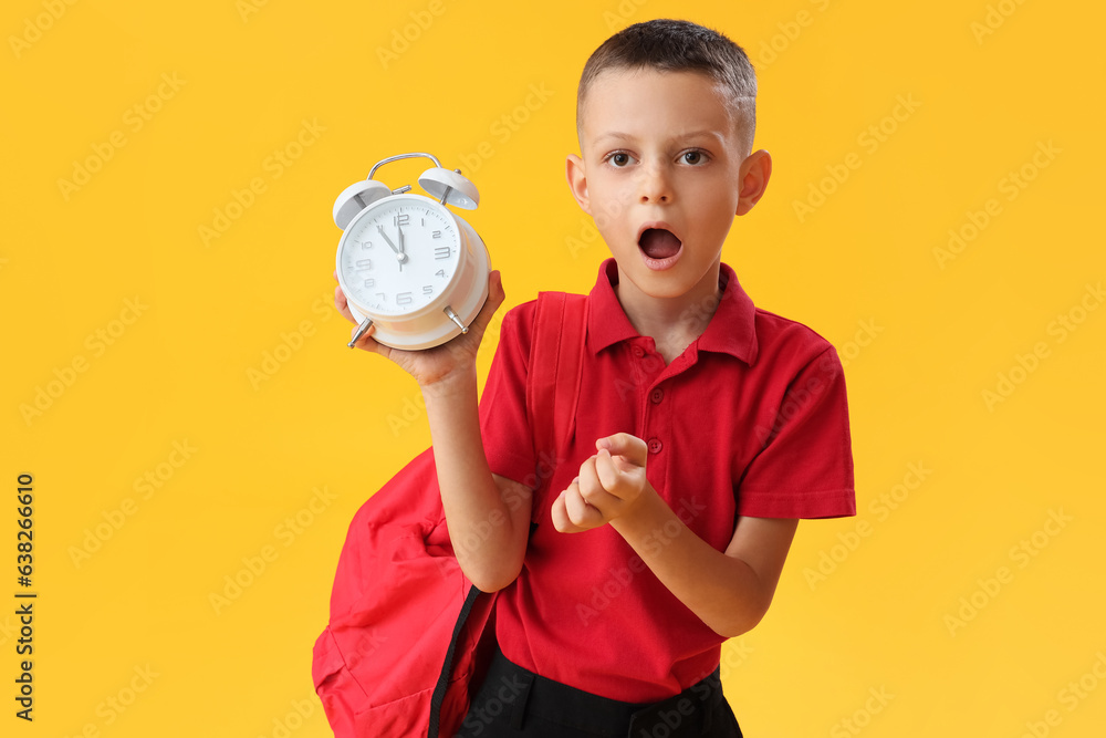 Surprised school boy with alarm clock on yellow background