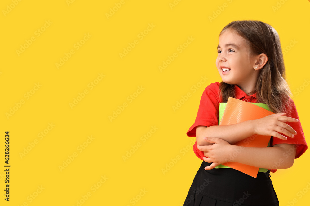 Little school girl with copybooks on yellow background